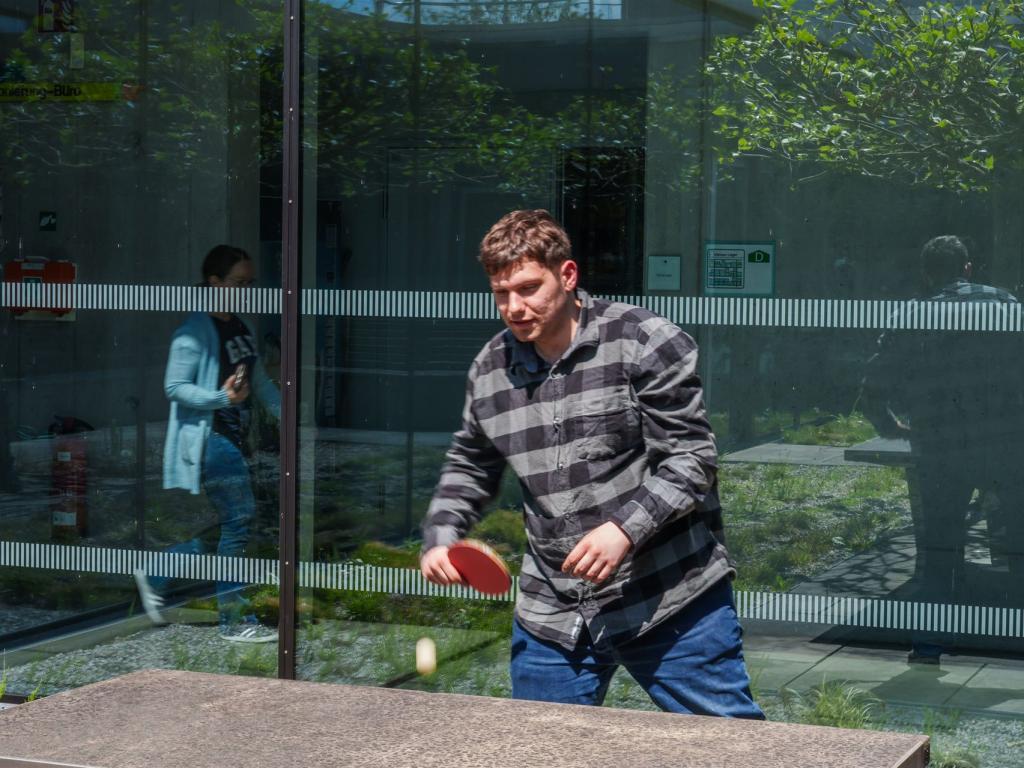 Man sieht einen Mann, welcher Tischtennis im Hof von Auwald72 spielt.