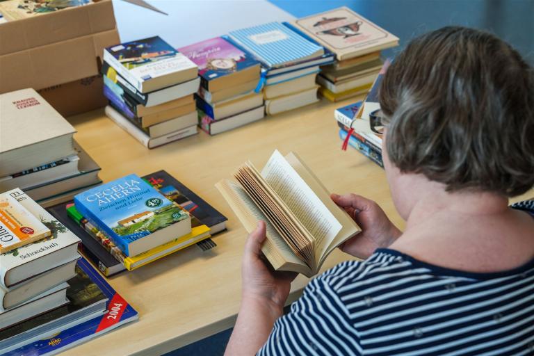 Man sieht eine Frau mit Büchern, die im Bereich Kommissionierung und Bürotätigkeiten arbeitet.